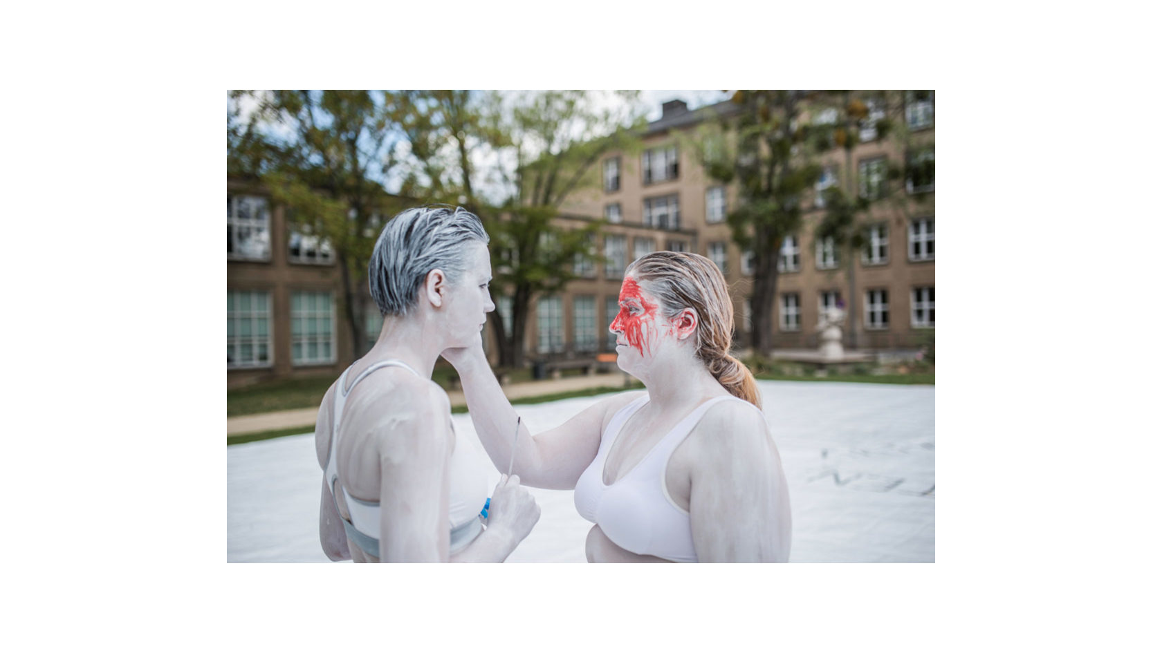 Bei den Orten des Miteinanders sind auf dem Campus der TU Dresden zwei Frauen am ganzen Körper mit weißer Farbe bemalt und berühren sich im Gesicht.
